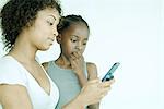 Mère et fille regardant vers le bas de téléphone portable ensemble, main de la jeune fille sur la bouche