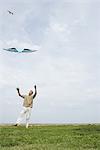 Man flying kite, arms raised, full length