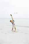 Young boy at the beach holding up shovel, throwing sand