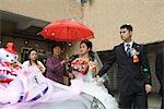 Chinese wedding, bride and groom leaving under confetti, bride covered by red parasol, decorated car in foreground