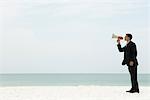 Businessman standing at the beach shouting into megaphone
