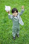 Little boy dressed in full suit holding up piggy bank