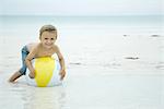 Little boy lying on top of beach ball at the beach, smiling at camera