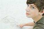 Teenage boy drawing car in sand, cropped view