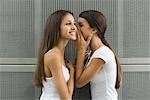 Teenage girl whispering in twin sister's ear, side view