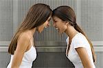 Teenage twin sisters leaning with foreheads touching, both shouting, side view