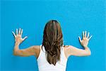 Frau stehend mit den Händen gegen blaue Wand, Rückansicht