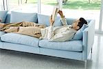 Homme couché sur le canapé, livre de lecture, vue latérale