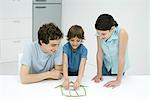 Little boy in kitchen with father and sister, building house out of green beans, all smiling