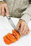 Woman slicing tomato with knife, cropped view