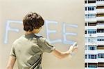 Teenage boy spray painting the word "free" on wall, rear view
