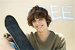 Teenage boy holding skateboard, smiling at camera, portrait