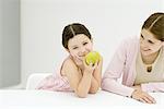 Kleines Mädchen sitzt am Tisch mit Mutter, Hand unter Kinn, Apfel, lächelnd in die Kamera halten