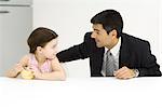 Father and daughter sitting at table, looking at each other, little girl eating cereal