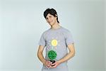 Young man wearing tee-shirt with sun graphic, holding potted plant, smiling at camera
