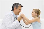 Doctor talking into stethoscope as little girl listens, both smiling
