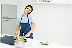 Young man cooking in kitchen, using cell phone