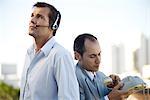 Two men standing back to back, one using headset, the other holding landline phone