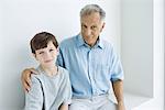 Grandfather sitting with arm around grandson's shoulder, both smiling at camera, portrait