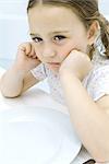 Little girl sulking at dinner table, close-up