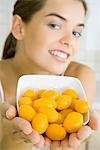 Young woman holding out bowl of yellow cherry tomatoes