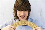 Young man holding protractor in both hands, smiling at camera