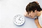 Young man lying on the ground next to clock, eyes closed