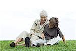 Grandmother and grandson sitting together outdoors, reading book