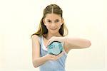 Preteen girl holding small globe in hands, smiling at camera