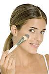 Woman applying face powder with make-up brush, smiling at camera