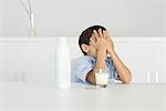 Boy with spilled milk, covering face with hands