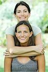 Mother standing behind teenage daughter, embracing her, both smiling at camera, portrait