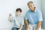 Grandfather sitting with grandson, smiling as grandson plays with toy airplane