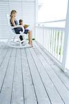 Femme assise dans le fauteuil à bascule sur le porche, lu l'histoire de petit garçon debout à côté d'elle