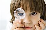 Little boy looking through magnifying glass at camera