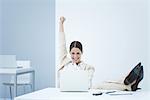 Young businesswoman sitting at desk, smiling at laptop and raising one arm in the air