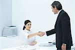 Professional woman sitting at desk, shaking hands with businessman