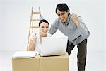 Young couple looking at laptop computer on top of cardboard box, smiling, clenching fists