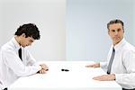 Businessmen sitting at table, tipped over chess piece between them