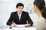 Businessman sitting at desk, talking with woman and smiling