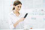 Woman standing at kitchen counter, looking at cell phone, smiling