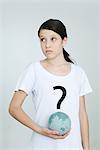 Girl wearing tee-shirt printed with question mark, holding globe, looking away