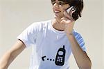 Adolescent portant tee-shirt imprimé avec graphique de téléphone cellulaire, à l'aide d'un téléphone cellulaire, souriant