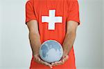 Man wearing Swiss flag tee-shirt, holding globe with both hands