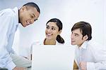 Young professionals sitting around laptop computer, leaning close together, smiling