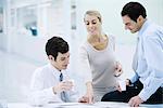 Three professionals taking a coffee break, woman pointing at newspaper