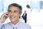 Businessman using cell phone in office, looking up, smiling