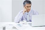 Businessman sitting at desk, looking at laptop computer, holding head