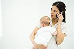 Mother holding infant, using cell phone