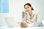 Professional woman touching infant lying on desk, making phone call